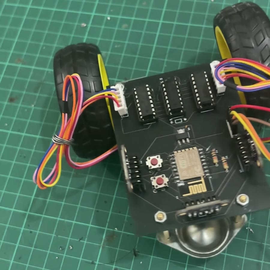The assembled Nanodot on a cutting mat: black PCB with the ESP-12E, three socketed chips, stepper cables looped to the side, two wheels and a metal ball caster